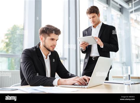 Two Concentrated Young Businessmen Working With Laptop And Tablet In