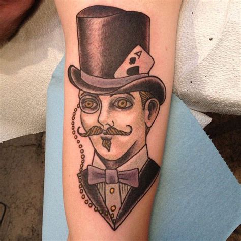 A Man With A Mustache And Top Hat Tattoo On His Arm Is Wearing A Chain