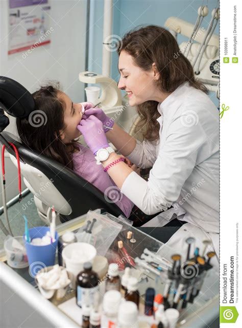 Young Female Dentist Is Treating Patient Girl Teeth At Dental Office