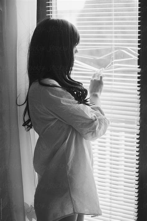 Black And White Photo Of A Young Woman Looking Through The Window By
