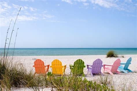 Colorful Adirondack Chairs Facing A White Sandy Beach Stock Photo