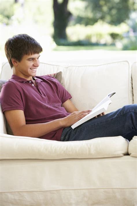 Teenage Boy Relaxing On Sofa At Home Reading Book Stock Photo Image