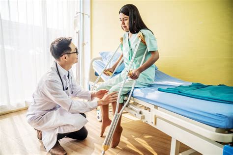 Asian Male Doctor Or Physiotherapist Examining Knee Female Patient