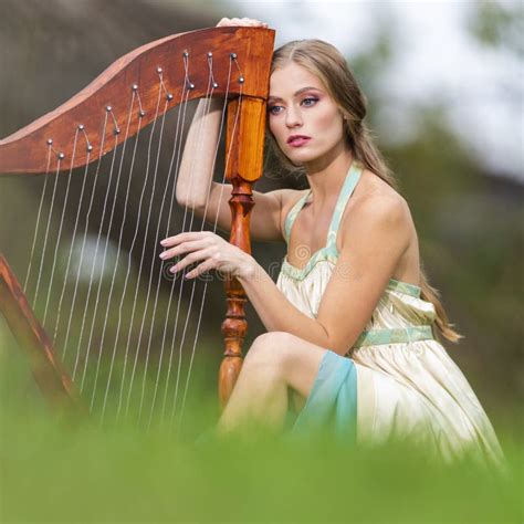 Portrait Of Relaxing Female Harpist Woman In Light Dress Playing The