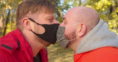 Влюбленная гей пара в коронавирусных масках для лица потирающая носы знакомства в парке