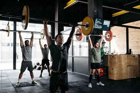 Group Of Strong Adult Guys Lifting Heavy Barbells Over Head During