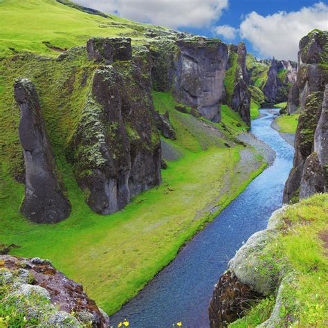 A River Flowing Through A Lush Green Valley Surrounded By Tall Rock