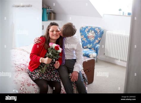 Loving Young Downs Syndrome Couple Sitting On Bed With Man Giving Woman