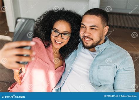 Positive Loving Couple Resting On Couch At Home And Taking Selfie On Smartphone Stock Image