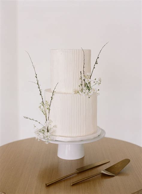 A White Wedding Cake Sitting On Top Of A Table Next To A Knife And Fork