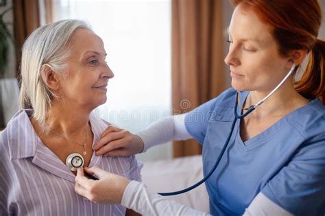 Nurse Examining Senior Patient With Stethoscope At Her Home Stock