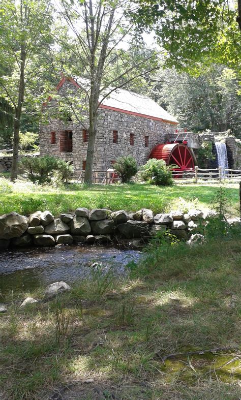 A Stone Building With A Red Water Wheel In The Back Ground And Trees