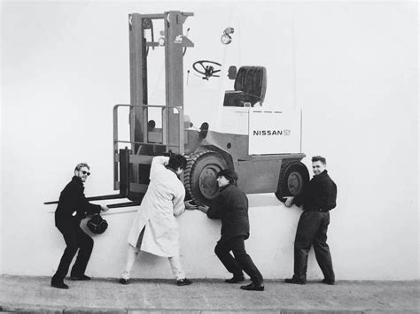 Three Men Standing Next To A Forklift On The Side Of A Building While