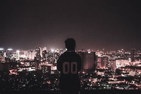 Photography Of A Person Watching Over City Lights During Night Time