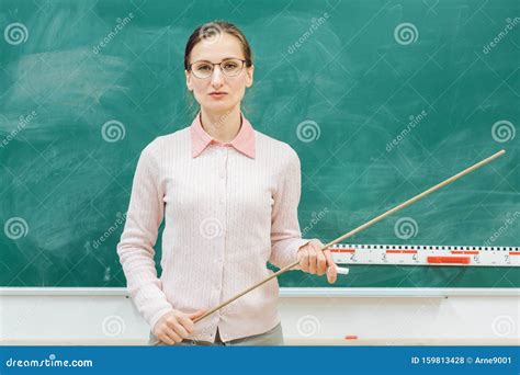 Strict Teacher Standing In Front Of Blackboard In Class Stock Photo