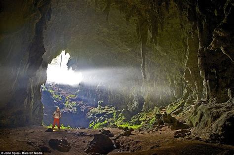 A Man Standing In The Middle Of A Cave With Light Coming From Its Entrance