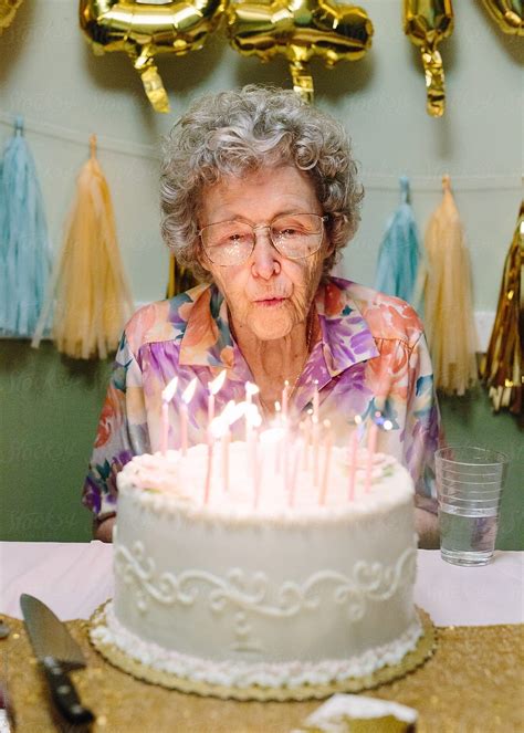 Elderly Woman Blowing Out Birthday Candles On Cake By Stocksy Contributor Cameron Zegers