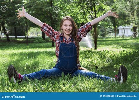 Beautiful Pregnant Woman In Denim Overalls Sitting On The Grass In The Park Stock Photo Image