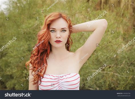 Young Redhead Model Wearing Strip Shirt Posing Outdoors With One Arm Up