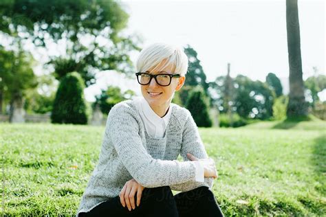 Blonde Woman Wearing Rimmed Glasses Sitting On The Park By Stocksy