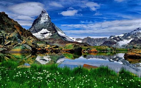 Sharp Mountain Peaks Of Rock Snow Lake Meadow With Green Grass Blue