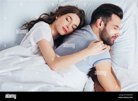 Young Couple Sleeping On Soft White Bedding In Bedroom While Woman