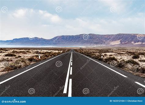 Long Straight Empty Asphalt Road Through Arid Landscape Against Ocean