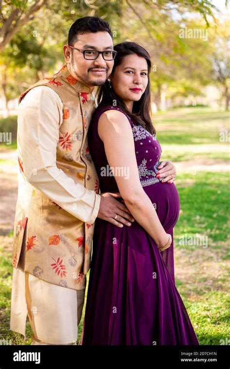 Young Asian Indian Pregnant Woman With Her Husband Wearing Traditional Outfit Standing In Park