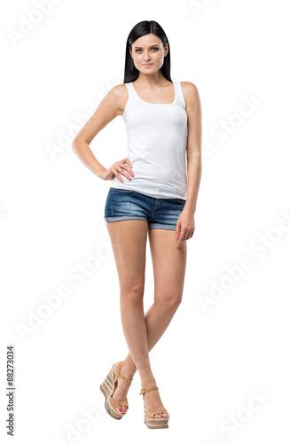 Full Length Portrait Of A Brunette Woman Who Is In A White Tank Top And Blue Denim Shorts