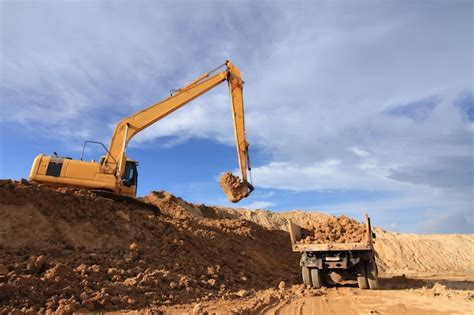 Excavador pesado que carga el camión de descargador con la arena en mina sobre el cielo azul