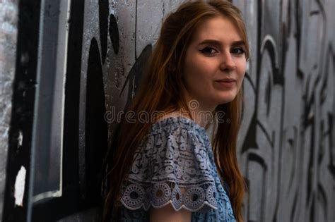 Smiling Young Woman Standing Near Gray Wall And Looking At Camera Stock