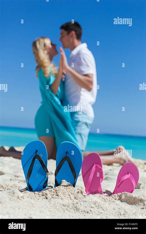 Pair Of Color Flip Flops On Sandy Beach Near Sea With Romantic Couple On Background Focus On