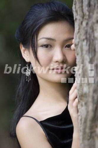 blickwinkel attraktive junge asiatin in schwarzem abendkleid hinter einem baum stehend
