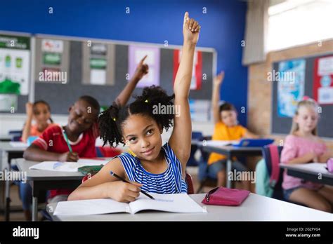 African American Girl Raising Her Hands While Sitting On Her Desk In