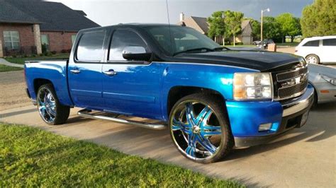 A Blue Truck Parked On The Side Of A Road Next To A Silver Car In Front