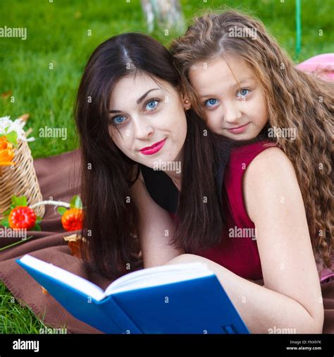 Mom And Daughter Reading A Book Lying On The Plaid In The Park Stock