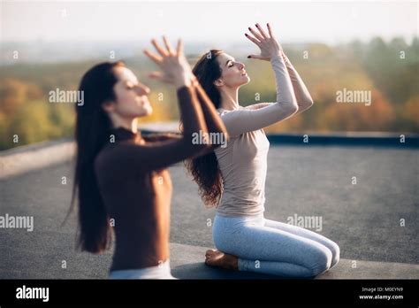 Two Young Beautiful Women Doing Yoga Asana Sitting In Vajrasana Exercise On The Roof Outdoor