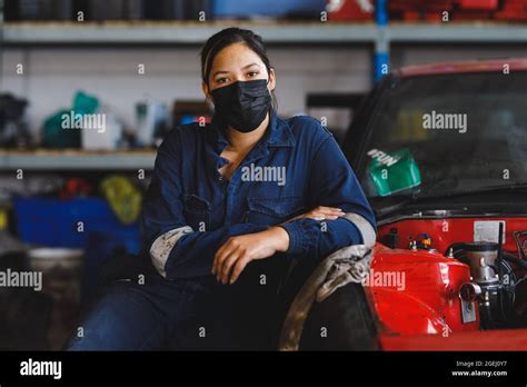 Mixed Race Female Car Mechanic Wearing Face Mask And Overalls Looking