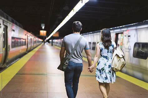 Young Couple Walking Hand In Hand In The Station By Stocksy