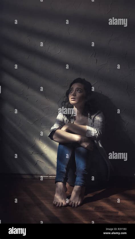 Young Sad Woman Sitting Alone On The Floor In An Empty Room In A Shadow