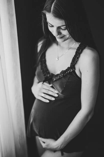 Беременная женщина держится за руки вокруг живота девушка обнимает круглый живот у окна дома