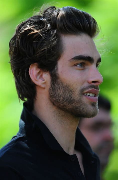 A Close Up Of A Person Wearing A Black Shirt And Hair In A Bun With A Beard