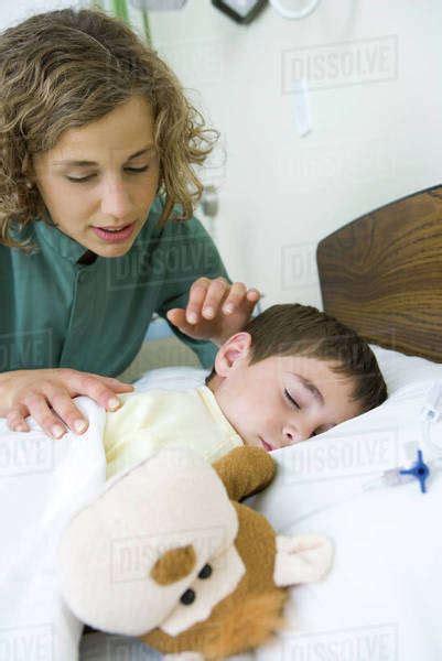 Boy Sleeping In Hospital Bed Intern Looking Over Boys Shoulder