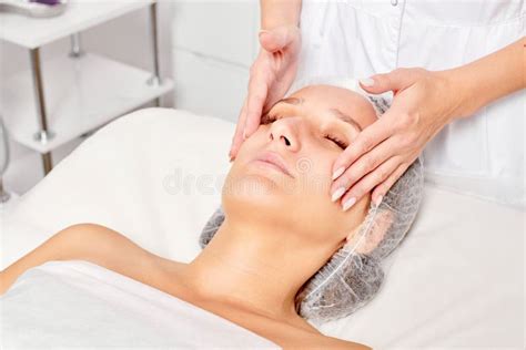 Beautician Massages Cream Mask Into Woman Face Skin For Rejuvenation Procedure In Beauty Salon