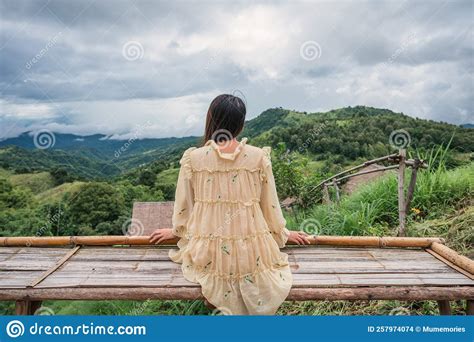 Asian Woman In Yellow Dress Sitting At Wooden Terrace Among The
