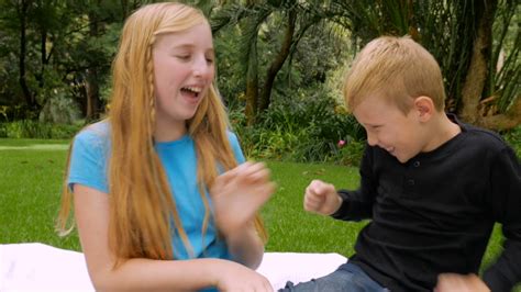 A Younger Brother And Older Sister Tickle Each Other Outside And Smile