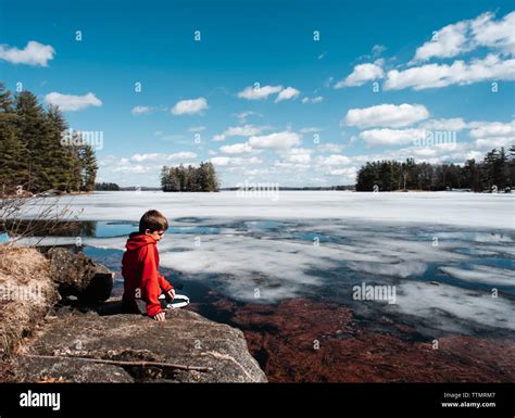 Boy Sitting On The Rocky Shore Of An Icy Lake During Spring Thaw Stock