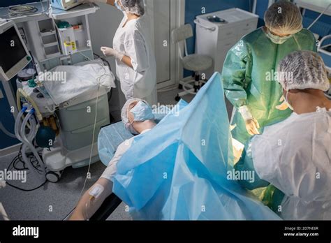 Patient Lying On Operation Table While Professional Surgeons Bending
