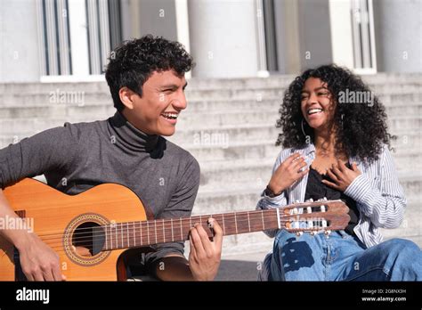 A Young Latin Couple Playing The Guitar And Laughing Sitting On Stairs
