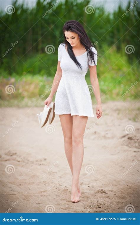 attraktiv brunettflicka med den korta vita klänningen som barfota strosar på bygdvägen ungt